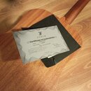 Fotografie zachycuje dřevěný povrch akustické kytary, na kterém leží černý obal a certifikát pravosti. Na dokumentu je logo a nápis FURCH, nadpis Cer…