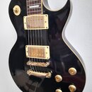 Černá elektrická kytara s gold hardwarem a krémovým lemováním. Na snímačích je nečitelný nápis. Kytara má dva humbuckery, Tune-o-matic můstek a čtyři…