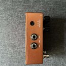 Fotografie zachycuje zadní stranu efekt pedálu v bronzové barvě. Jsou zde vidět tři konektory a nápisy 9VDC 100mA, MONO OUT a STEREO. Na pravé straně…