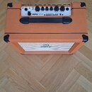 Kytarový kombozesilovač v oranžovém vinylu s černými plastovými rohy a úchytem. Na horním ovládacím panelu je bílý nápis ORANGE CRUSH 20 a řada ovlád…