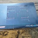Fotografie znázorňuje kartónovou krabici s obrázkem DJ kontroléru. Na krabici je vlevo nápis GET READY TO REMIX a vpravo dole modelové označení JOCKE…