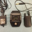 Na fotografii je černý bezdrátový systém značky SHURE, který tvoří přijímač, vysílač s anténou a napájecí adaptér. Přijímač má digitální displej, ovl…