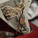 Fotografie zachycuje vnitřní elektroniku elektrického nástroje s červeným lakovaným tělem a bílou plastovou deskou. Je vidět kovová deska s připevněn…