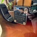 Detailní pohled na kovovou kostku u základny krku elektrického nástroje. Na chromovaném povrchu je vyryto logo Fender a nápis PLAYER PLUS. Kostka je…