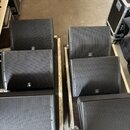 Šest černých reproduktorových beden s kovovými mřížkami, rozmístěných ve dvou řadách na dřevěných podvozech. Každý reproduktor má v dolní části dopře…