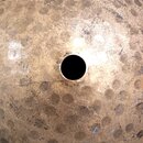 Detailní pohled na povrch kovového nástroje, pravděpodobně činely nebo gongu, v zlatavé barvě. Povrch je zdobný pravidelnými kovem vykovanými důlky a…
