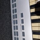 Detailní pohled na ovládací panel stříbrného klávesového nástroje s bílými a černými klávesami. Na panelu jsou šedé tlačítka s nápisy DIRECT PATCH SE…