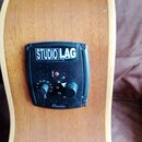 Detail na ovládací panel akustické kytary s dřevěným povrchem. Černý plastový panel nese bílý nápis STUDIO LAG System a v dolní části nápis Shadow. P…