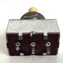 Fotografie znázorňuje elektronický potenciometr s kovovým tělem a béžovým knoflíkem. Na spodní straně je vidět hnědý bakelitový základ s třemi připáj…