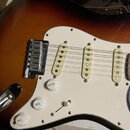 Detail elektrické kytary s t bodies v barvě sunburst a bílým pickguardem. Nástroj má tři jednosmyčkové snímače s krémovými kryty, chromovaný kobylník…