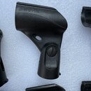 Černý plastový držák na mikrofon s nápisem SHURE vyraženým do materiálu. Předmět má v horní části plochou hlavu a spodní cylindrický úchop s viditeln…