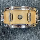 Fotografie znázorňuje snare drum s dřevěným korpusem v přírodní světle barvě a chromovaným obručemi. Uprostřed korpusu je umístěno kulaté logo s nápi…