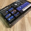 Fotografie zachycuje kartonovou krabici od syntetizátoru. Na povrchu je vidět nápis MININOVA SYNTHESIZER a obrázky modrého nástroje s klávesnicí. Kra…