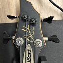 Hlava basové kytary v černé barvě s přirozeným dřevěným lemováním. Na čelní straně je zlatý nápis „Curbow Bass“ a vedle něj stylizovaný podpis. Na ho…