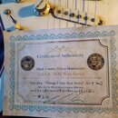 Fotografie zachycuje detail elektrické kytary s bílým pickguardem a dvěma knoflíky s nápisy TONE a VOLUME. Na kytaru je položen papírový Certificate…