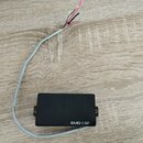 Černý elektrický snímač s obdélníkovým tvarem a dvěma montážními šrouby po stranách. Na spodní hraně je bílý nápis EMG-ESP. Ze snímače vede šedý kabe…