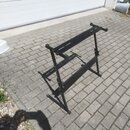 Černý kovový stojan na klávesové nástroje v rozloženém stavu. Stojan má X-tvarovou konstrukci s nastavitelnou výškou a horní opěrnou lištou. Povrch j…