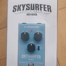 Fotografie zobrazuje bílou krabici s modrým efekt pedálem. Na krabici i na pedálu je uveden nápis SKYSURFER REVERB a značka tc electronic. Pedál má t…