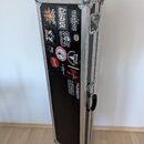 Černý transportní flightcase s hliníkovými hranami a kovovými rohy. Přední strana je polepena různými nálepkami, mezi nimiž jsou čitelné nápisy "Deat…