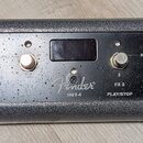 Černý kytarový efekt pedál s texturovaným povrchem. Na přístroji je bílý nápis Fender a model MGT-4, v pravém horním rohu je označení ASSY. P/N 77102…