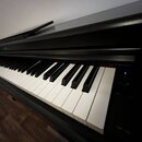 Černý digitální piano s bílými a černými klávesami. Na pravé straně je viditelný nápis YDP-165 a ovládací prvky s označením MIN a MAX. Nástroj je umí…