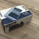 Bílá papírová krabice s modrými prvky, na které je zobrazen efekt pedál. Na krabici jsou viditelné nápisy GRUNGE DISTORTION a logo Digitech. Povrch k…
