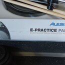 Bílá krabice s produktem Alesis E-PRACTICE PAD ELECTRONIC DRUM PRACTICE PAD. Na krabici je zobrazen obrázek černého elektronického tréninkového padu…