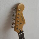 Fotografie zachycuje hlavu elektrické kytary z přírodního světlého dřeva s chromovanými ladičkami. Na povrchu je černý nápis Squier JAZZMASTER s drob…