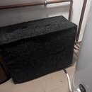 Černý obdélníkový box potažený hrubým textilem připomínajícím kobercovinu. Na horní straně jsou dvě černé úchytky. Na povrchu nejsou vidět žádné znač…