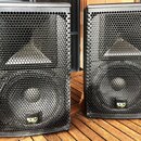 Dva černé reproduktory s kovovými mřížkami včelí struktury. Na spodní části obou reproduktorů je umístěno žluté a bílé logo s nápisem KV audio. Povrc…