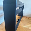 Černý digitální piano v černém stojanu. Na horní liště je vidět bílý nápis Korg. Nástroj má v dolní části pedály a je umístěn na dřevěné podlaze. Pov…