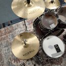 Fotografie zachycuje část bicí sady s červenými kotli a bílými koženmi značky EVANS a REMO. Na činelech je vidět logo a nápis istanbul Agop music in…