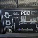 Černá pasivní DI box s nápisem PDB Passive Direct Box. Na spodní straně je schéma zapojení s označením vstupů INPUT a IN/THRU, TRANSFORMER, ATTENUATO…