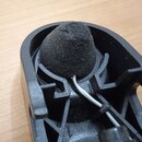 Černý plastový držák s integrovanou černou pěnovou clonou ve tvaru kužálu. Z držáku vede bílý kabel upevněný černou stahovací spojkou. Povrch plastu…