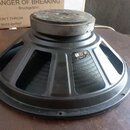 Černý reproduktor s kovovým rámem a magnetem v horní části. Na rámu je viditelný malý kovový štítek s nečitelným nápisem. Povrch magnetu vykazuje zná…