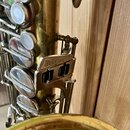 Detail zlatavého saxofonu s viditelným opotřebením laku a drobnými škrábancemi. Na kovovém držáku je vyryt nápis Wellklang. Jsou vidět klapy s perleť…