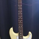 Elektrická kytara s krémovým korpusem, bílým pickguardem a hnedou hmatníkovou deskou. Na hlavě je černý nápis „Fender STRATOCASTER“. Nástroj má tři s…