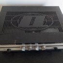 Černý elektronický přístroj s mřížkou na horní straně, ve které je vyřezáno logo znázornující stylizované písmeno „N“. Na předním panelu je vpravo ná…