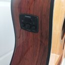 Detailní pohled na bok akustické kytary s hnědým lakovaným povrchem z dřeva. V těle je osazený černý ovládací panel s nápisem FISHMAN. Panel obsahuje…