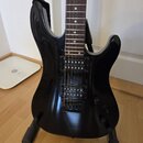 Černá elektrická kytara s tmavým hnedým hmatníkem a bílými tečkovými značkami. Nástroj má dva snímače typu humbucker a dva ovládací knoflíky. Povrch…