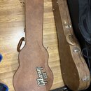 Dvě hnědé kytarové pouzdra z texturovaného materiálu položená na dřevěné podlaze. Na levém pouzdře je vidět nápis Gibson USA. Pravé pouzdro vykazuje…