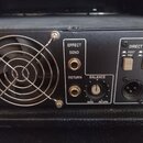 Detail zadní strany černého zesilovače s kovovým chladicím ventilátorem a mřížkou. Na panelu jsou vstupy EFFECT SEND a RETURN, ovladač BALANCE s nápi…