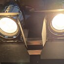 Dvě zapálené studiové lampy s černými kovovými clony (barn doors). Světla jsou umístěna vedle sebe na kovové liště. Na přístrojích nejsou viditelné ž…