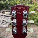 Fotografie zachycuje hlavu elektrické kytary v tmavě červené barvě. V horní části je vyrazeno sériové číslo 017160726 a pod ním nápis .MADE IN U.S.A.…