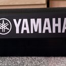 Černý plastový reproduktor s horní mřížkou. Na přední straně je bílé logo a nápis YAMAHA. Povrch plastu vykazuje drobné nečistoty a prach.