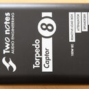 Černý kovový box s matným povrchem. Na horní straně jsou bílé nápisy „Two notes AUDIO ENGINEERING“ s logem, „Torpedo Captor 8“ a „100W 8Ω“. Vedle jso…