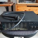 Černý rackový zesilovač s kovovým šasi a perforovaným zadním panelem. Na levé straně je štítek s nápisy „MODEL: KR-100“, „MADE IN GERMANY“ a „CE“. Vp…