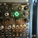 Černý modulární syntetizátor s nápisem SWORDS v horní části a logem behringer ve spodní. Zařízení obsahuje řadu černých a bílých otočných ovladačů s…