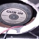 Fotografie zachycuje zadní část reproduktoru umístěného v černém boxu. Na magnetu je bílý štítek s nápisy CELESTION, G12H-100, TYPE NO. T35A7 a IMPED…