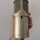 Stříbrný kondenzátorový mikrofon s kovovou síťkou a cylindrickým tělem. Na přední straně jsou umístěny dva přepínače s označením symbolů pro kardioid…